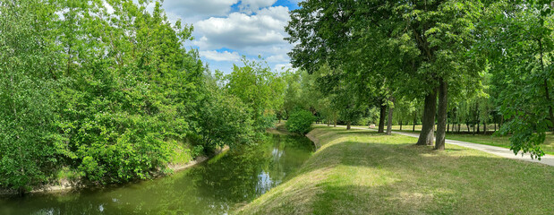 green park landscape with water canal and walking path on bank. panoramic image.