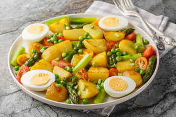 Delicious salad of potatoes, asparagus, cherry tomatoes, eggs and green peas close-up in a plate on...