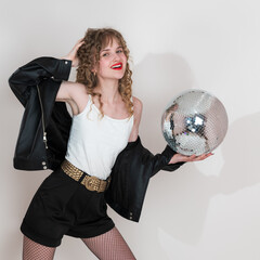 Happy young woman dancer who is absolutely beaming with joy. She is holding mirror disco ball and looking directly at camera. Young adult pin-up girl with curly hair and she is dressed for clubbing
