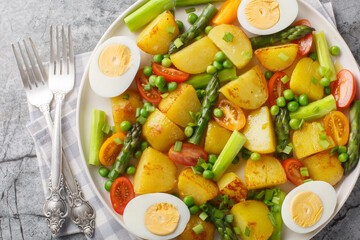 Delicious salad of potatoes, asparagus, cherry tomatoes, eggs and green peas close-up in a plate on the table. Horizontal top view from above