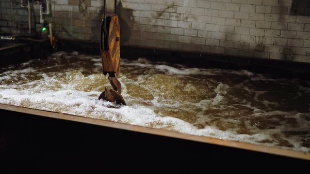 Crane hook stirs turbulent frothy water in a quench tank at a steel manufacturing foundry