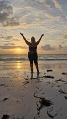 Frau mit Glück und Freude bei Sonnenaufgang am Strand mit Händen nach oben