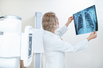 A female doctor looks at an x-ray of the ribs and lungs against the background of x-ray equipment....