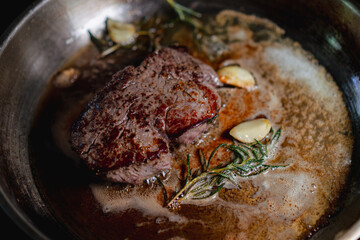 Steak cooking in stainless steal pan with garlic and rosemary 