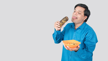A young man looks desperate to eat a cob of corn in his hand and is showing his tongue with his crazy facial expression.