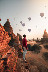 Man  stands watching balloons float at Bagan temple in Myanmar archaeological zone in the morning.