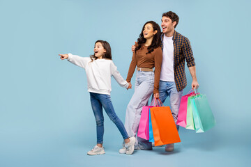 Seasonal sales. Family holding colorful paper shopper bags, girl pointing aside at free space, standing on blue background