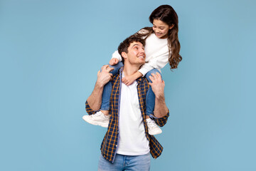 Father's love. Happy daddy carrying his daughter on shoulders posing and having fun on blue studio...