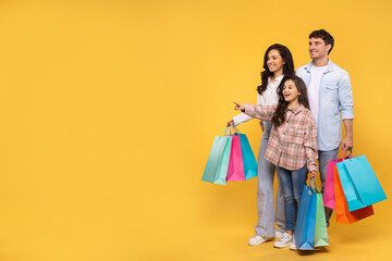 Shopping offer. European family with daughter carrying shopper bags and pointing at free space over...