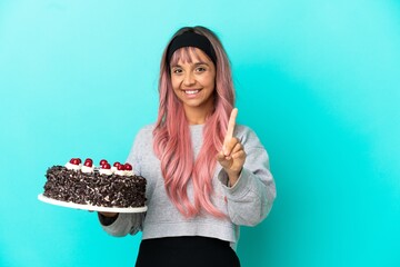 Young woman with pink hair holding birthday cake isolated on blue background showing and lifting a...