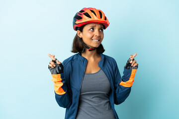 Young cyclist woman isolated on blue background with fingers crossing and wishing the best