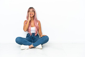Young mixed race woman with pink hair sitting on the floor isolated on white background shouting with mouth wide open