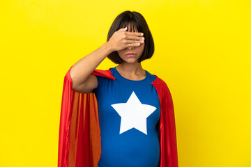 Super Hero pregnant woman isolated on yellow background covering eyes by hands. Do not want to see something