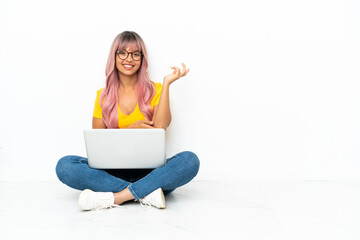 Young mixed race woman with a laptop with pink hair sitting on the floor isolated on white...