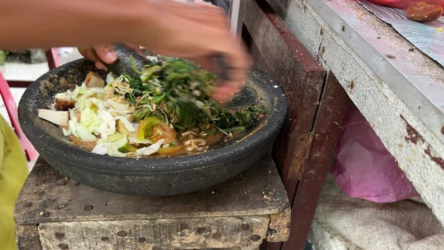 A street food seller making Indonesian traditional dish named Lotek which is made from many kinds of vegetable and peanut sauce with stone mortar and pestle