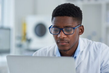 Science, reading and black man with laptop, glasses pharmaceutical research in laboratory. Medical study, lab technician or scientist on computer for online review, report or checking results on web.