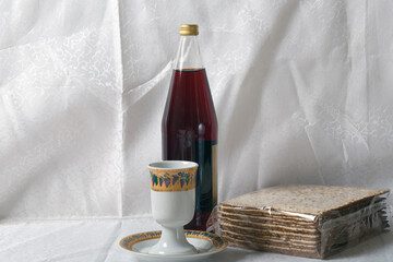 Package of matzah, a Kiddush cup, and a bottle of grape juice against a backdrop of white lace...