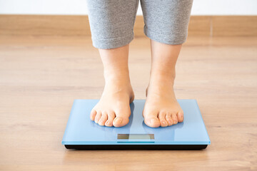 Closeup of a young woman weighing herself on a scale at home