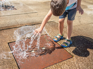 A child play in the square with the water from the fountain on a sunny summer day.Active summer...