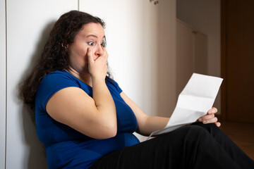 Sad woman complaining reading a letter in the night sitting on a floor at home