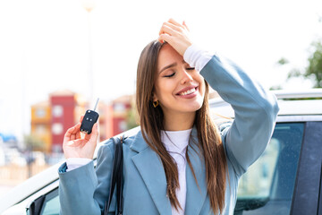Young pretty woman holding car keys at outdoors has realized something and intending the solution - obrazy, fototapety, plakaty