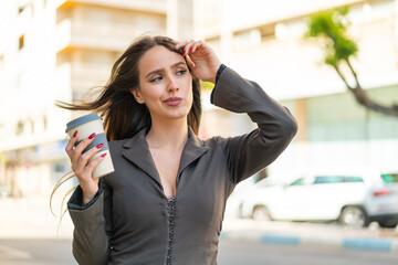 Young woman holding a take away coffee at outdoors having doubts and with confuse face expression