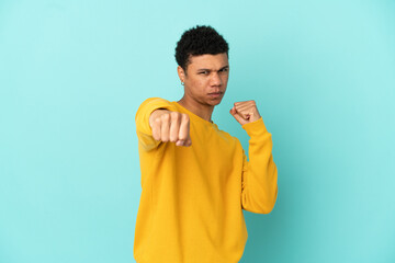 Young African American man isolated on blue background with fighting gesture