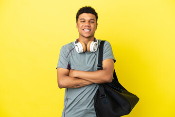 Young sport African American man with sport bag isolated on yellow background keeping the arms...