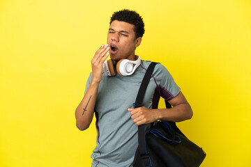 Young sport African American man with sport bag isolated on yellow background yawning and covering...
