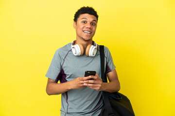 Young sport African American man with sport bag isolated on yellow background surprised and sending...