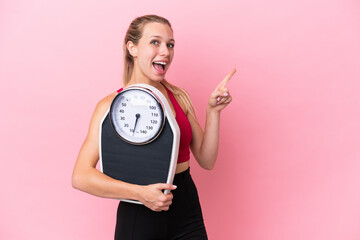 Young caucasian woman isolated on pink background with weighing machine