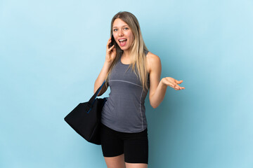 Young sport woman with sport bag isolated on blue background keeping a conversation with the mobile...
