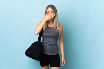 Young sport woman with sport bag isolated on blue background covering mouth with hand