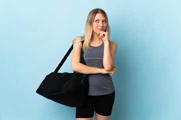 Young sport woman with sport bag isolated on blue background thinking an idea while looking up