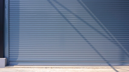 Automatic gray roller shutter entrance door of industrial warehouse building with sunlight and...