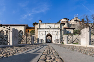 The perspective from ground level leads through a cobbled pathway to Brescia castle entrance, where...
