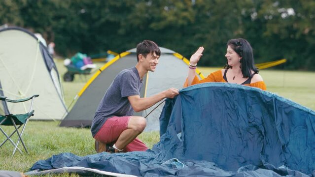 Young couple giving each other high five after reading instructions and setting up tent for camping at outdoor summer music festival - shot in slow motion