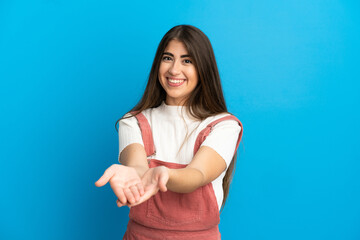 Young caucasian woman isolated on blue background holding copyspace imaginary on the palm to insert...