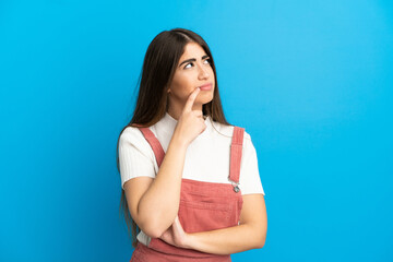 Young caucasian woman isolated on blue background having doubts while looking up