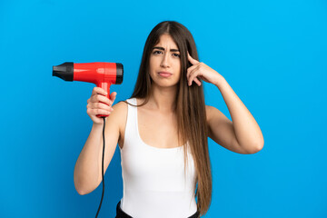 Young caucasian woman holding a hairdryer isolated on blue background having doubts and thinking