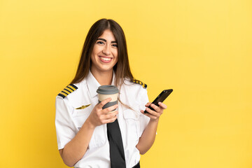 Airplane pilot isolated on yellow background holding coffee to take away and a mobile