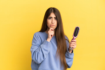 Young caucasian woman holding hairbrush isolated on blue background having doubts and thinking