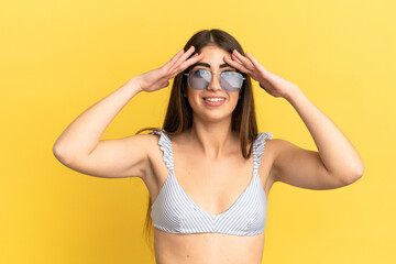 Young caucasian woman in swimsuit in summer holidays isolated on yellow background with surprise...