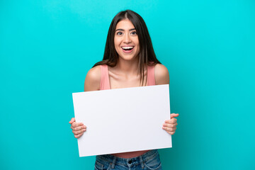 Young caucasian woman isolated on blue background holding an empty placard with happy expression