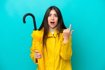Young caucasian woman with rainproof coat and umbrella isolated on blue background intending to...