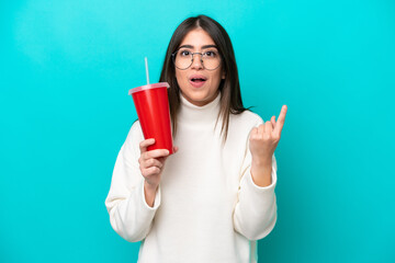 Young caucasian woman drinking soda isolated on blue background intending to realizes the solution while lifting a finger up - obrazy, fototapety, plakaty