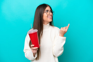 Young caucasian woman drinking soda isolated on blue background pointing up a great idea