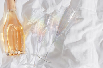 Rainbow color shining champagne glasses and white sparkling wine bottle on bed, on white blanket...