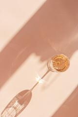 One wineglass with white wine sparkling at sunlight, beige background with dark shadow and reflection, sun flare light on table. Alcohol drink with star filter, top view, neutral pastel color