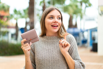 Young pretty blonde woman holding a wallet at outdoors intending to realizes the solution while lifting a finger up - obrazy, fototapety, plakaty